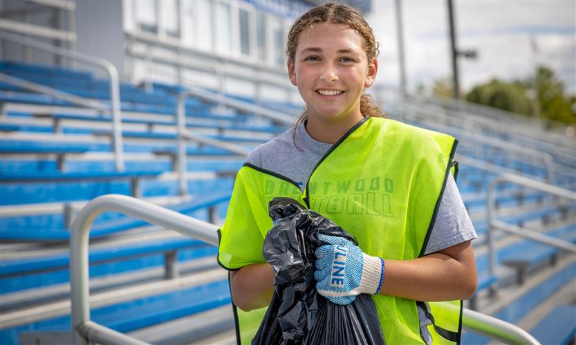 A softball player smiles while earing a neon vest